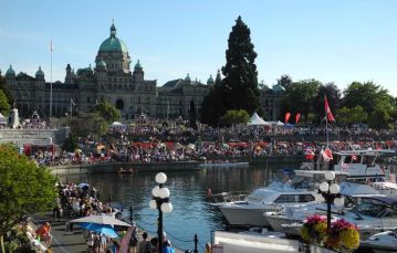 Large crowd gathers for cultural event at inner harbor in downtown Victoria with parliament buildings in background